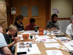 parents and childrens painting flower pots around a table.