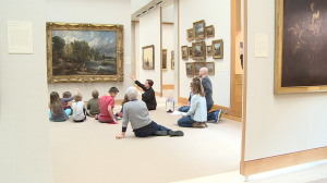 kids and adults sitting on floor looking up at landscape painting