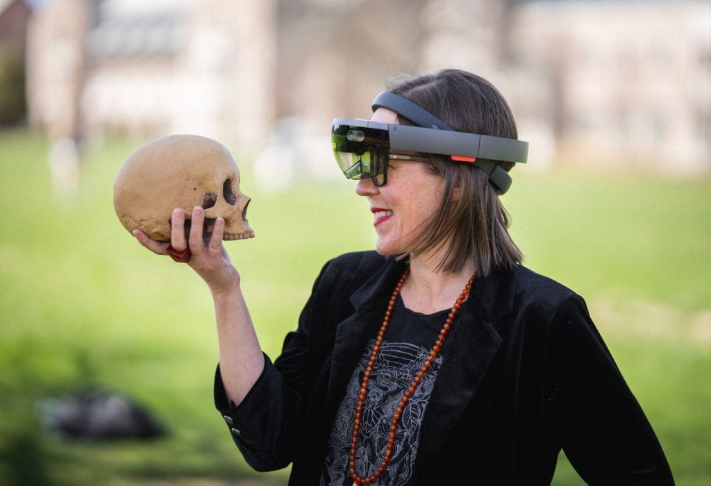 Professor Elizabeth Hunter in profile holding and looking at a skull. She wears virtual reality glasses.