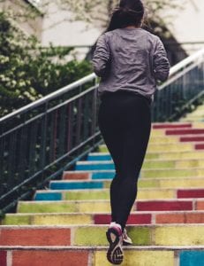 A woman running up colorful stairs in sneakers and exercise clothes.